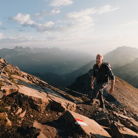 Mann beim Aufstieg zum Gipfel in der Morgensonne | © TVB Wipptal | Johannes Bitter