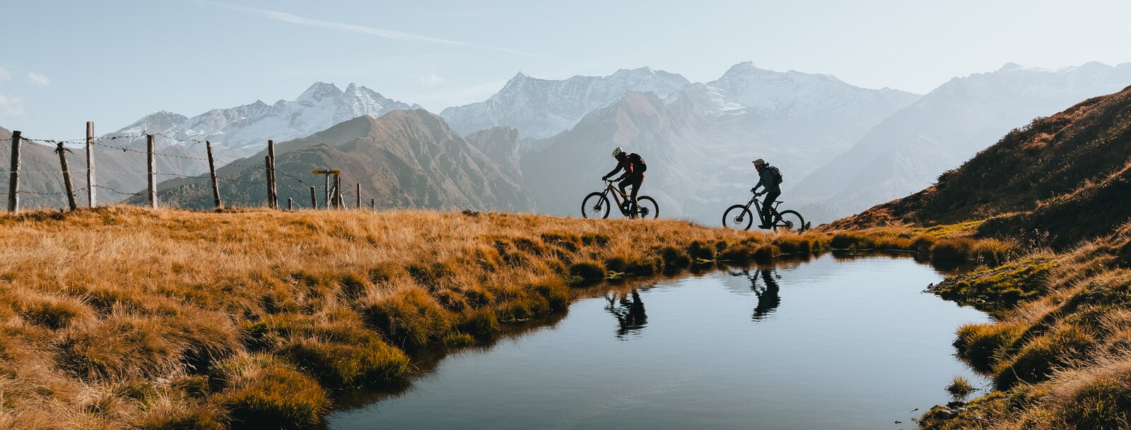 Zwei Mountainbiker fahren am Brenner Grenzkamm mit See im Vordergrund | © Mountainbiken im Herbst am Brenner Grenzkamm bei Gries