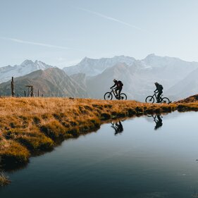 Zwei Mountainbiker fahren am Brenner Grenzkamm mit See im Vordergrund | © Mountainbiken im Herbst am Brenner Grenzkamm bei Gries