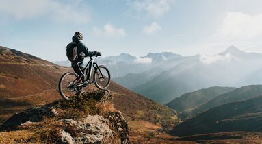 Mountainbiker mit Bike am Felsen mit Blick hinunter vom Brenner Grenzkamm | © TVB Wipptal | Johannes Bitter