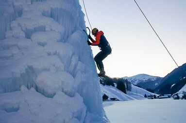 Ein Eiskletterer hängt mit seinen Eisgeräten am Eisturm | © Christoph Staud