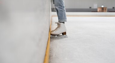 Zwei Eisläuferbeine in Schlittschuhen stehen am Eis an der Bande | © Kelli Mcclintock_unsplash