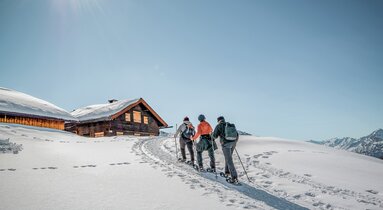 Eine Kleingruppe wandert mit Schneeschuhen zu einer Hütte | © TVB Wipptal | Judith Hammer