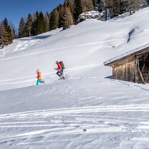 Ein Mädchen läuft mit ihren Schneeschuhen in tief verschneiter Landschaft, gefolgt von ihrem Vater | © Ewelina Herzog