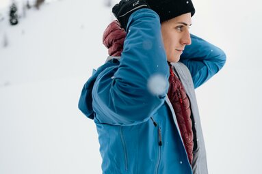 Ein Mann steht in einer Winterlandschaft und zieht sich eine Hardshelljacke an. | © TVB Wipptal | Johannes Bitter