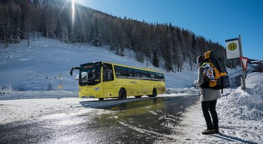 Eine Frau wartet mit Rucksack auf den kommenden Skibus | © Tirol Werbung | Sebastian Höhn