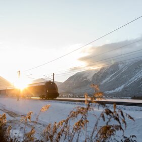 Ein Zug fährt in der Dämmerung durch eine Winterlandschaft | © Tirol Werbung | Robert Silz