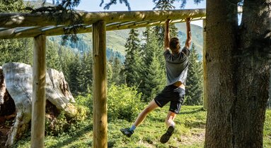 Ein Mann hangelt sich im Fitnessparcours über Metallstangen den Hügel hinauf | © TVB Wipptal | Helena Beermeister