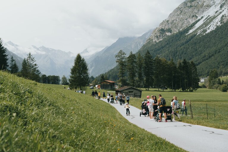 Mehrere Gruppen von Menschen spazieren einen asphaltierten Talweg zwischen Wiesen entlang | © TVB Wipptal | Johannes Bitter