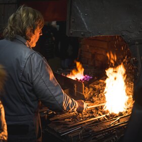 Ein Schmied steht vor der Esse mit offenen Feuer | © Kreativstadl