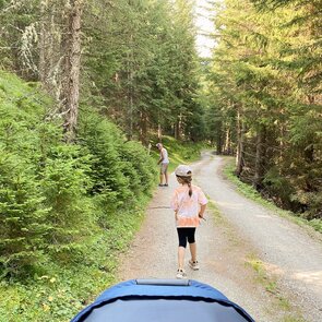 Ein Forstweg im Wald an dem ein Mann und ein Mädchen entlang spazieren | © Daniela Plattner