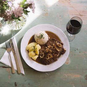 Teller mit Gulasch, Reis und Kartoffel und einer Vase mit Wiesenblumen | © TVB Wipptal / Tirol Werbung