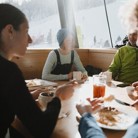 Vier Personen sitzen an einem Tisch vor einem Panoramfenster | © TVB Wipptal | Johannes Bitter
