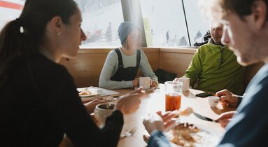 Vier Personen sitzen an einem Tisch vor einem Panoramfenster | © TVB Wipptal | Johannes Bitter