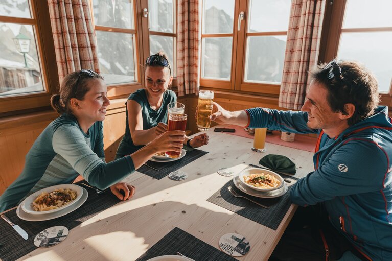 Drei Persone essen auf der Geraerhütte und stoßen mit Bier an | © TVB Wipptal / Johannes Bitter