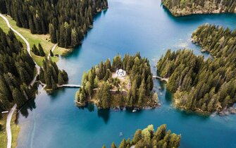 Drohnenaufnahme von einer Kapelle auf einer Insel inmitten eines Bergsees | © Marco Reimair