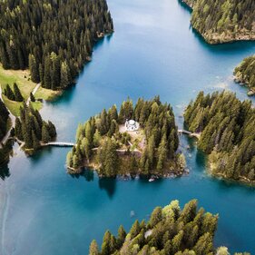 Drohnenaufnahme von einer Kapelle auf einer Insel inmitten eines Bergsees | © Marco Reimair