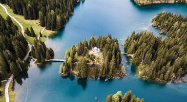 Drohnenaufnahme von einer Kapelle auf einer Insel inmitten eines Bergsees | © Marco Reimair