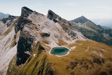 Ein Bergsee am Fuß von markanten Bergspitzen, aufgenommen aus der Vogelperspektive | © TVB Wipptal | Johannes Bitter