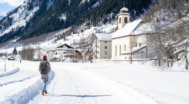 Frau spaziert neben der Loipe bei der Kirche in Gschnitz | © TVB Wipptal | Helena Beermeister